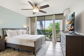 Ein Schlafzimmer mit Bett, Deckenventilator, Fernseher, Kommode und Balkon mit Blick.