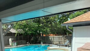 Un patio trasero con piscina, un porche techado y una cerca de madera.