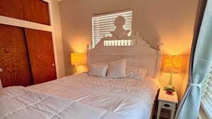 Ein ordentlich bezogenes Bett mit Kopfteil, zwei Nachttische mit Lampen und ein Fenster mit Vorhängen.