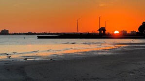Ein Strand bei Sonnenuntergang mit einem Steg und einem kleinen Gebäude.