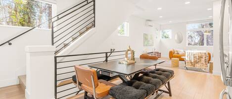 Un intérieur moderne comprenant un escalier, un coin repas avec une table et des chaises, un canapé et un banc.