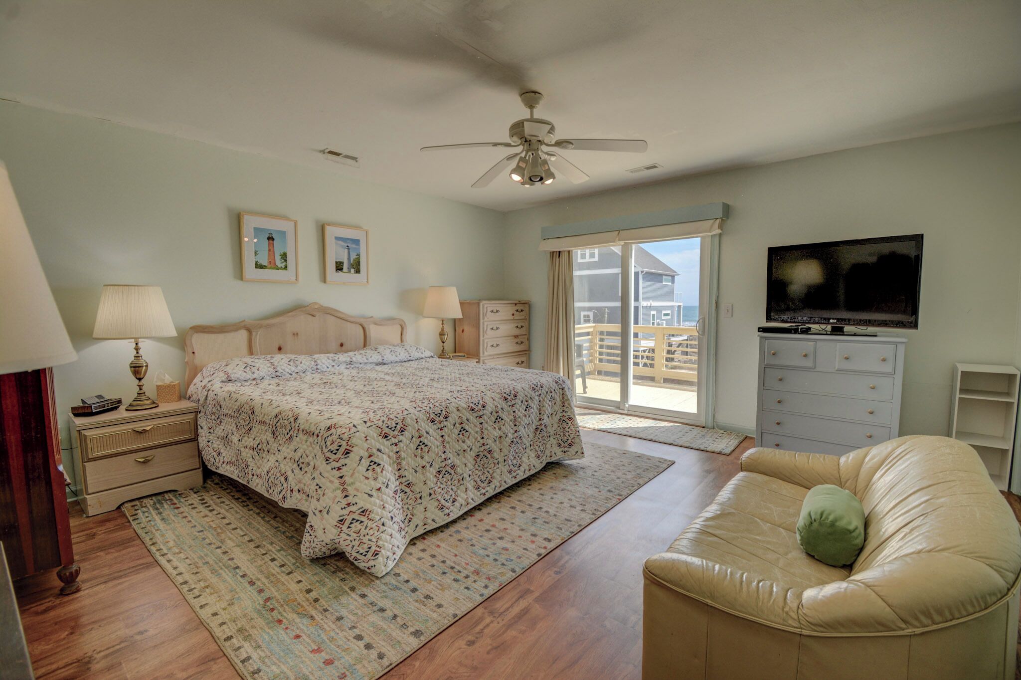 A bedroom with a bed, a ceiling fan, a TV, a dresser, and a window.