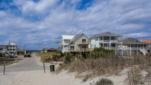 A coastal road leading to a beachfront property with multiple houses, a sandy path, and a clear sky. - Charming 4-Bedroom Home with Ocean Views in Topsail Beach! (Topsail Beach)
