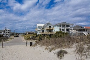 A coastal road leading to a beachfront property with multiple houses, a sandy path, and a clear sky. - Charming 4-Bedroom Home with Ocean Views in Topsail Beach! (Topsail Beach)