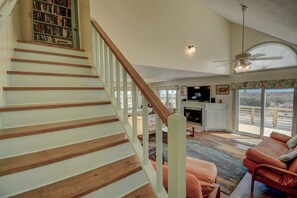 A staircase with wooden steps and white railings leading to a living area with a fireplace, a television, and a large window with a view. - Charming 4-Bedroom Home with Ocean Views in Topsail Beach! (Topsail Beach)