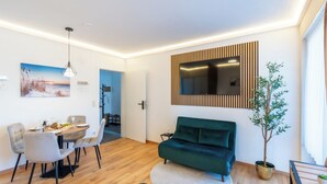 Een moderne woonkamer met een eethoek, een groene bank, een flatscreen televisie en een potplant.