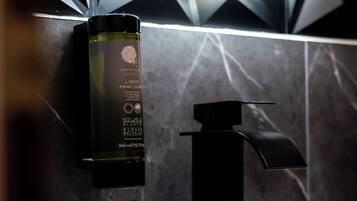A bathroom with a modern sink, a black faucet, and a bottle of liquid soap on the wall.