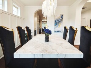 A dining room with a marble table, black upholstered chairs with gold accents, a chandelier, and a painting on the wall.