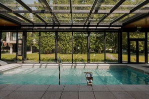 A swimming pool with a glass ceiling, surrounded by a garden and a view of buildings. - Nature-Inspired Sanctuary w/ 2 Pools, Garden & Free Bfast| 4.8 Mi to RCU Airport (Río Cuarto)