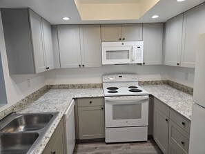 A kitchen with white cabinets, a microwave, a stove, and a double sink. - 2-BR Apt in Deerfield Beach with AC, Free wifi and Free parking near Golf Course (Deerfield Beach)