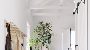A hallway with a bench, a potted plant, a door, and a wall-mounted rack with items. - open plan contemporary barn in the heart of Daylesford (Daylesford)