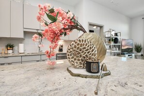Eine moderne Küche mit Marmorarbeitsplatte, einer dekorativen Vase mit rosa Blumen und einem einzigartigen, wabenartigen Behälter.