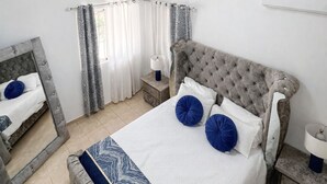 A bedroom with a bed, a nightstand, a mirror, a ceiling fan, and a window with curtains.