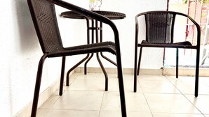 Dos sillas de mimbre con estructura de metal, una mesita redonda y un jarrón con flores amarillas.