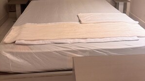 A neatly made bed with white linens, a headboard with vertical lines, and a plain wall with a subtle pattern.