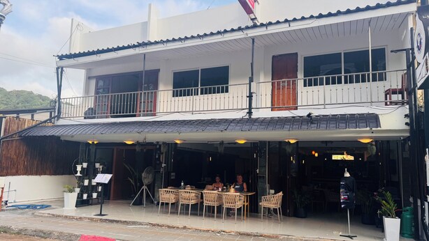 A two-story building with a balcony, outdoor seating area, and a signboard.