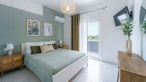 Een slaapkamer met een bed, nachtkastjes, een televisie, een plant en uitzicht op het landschap.