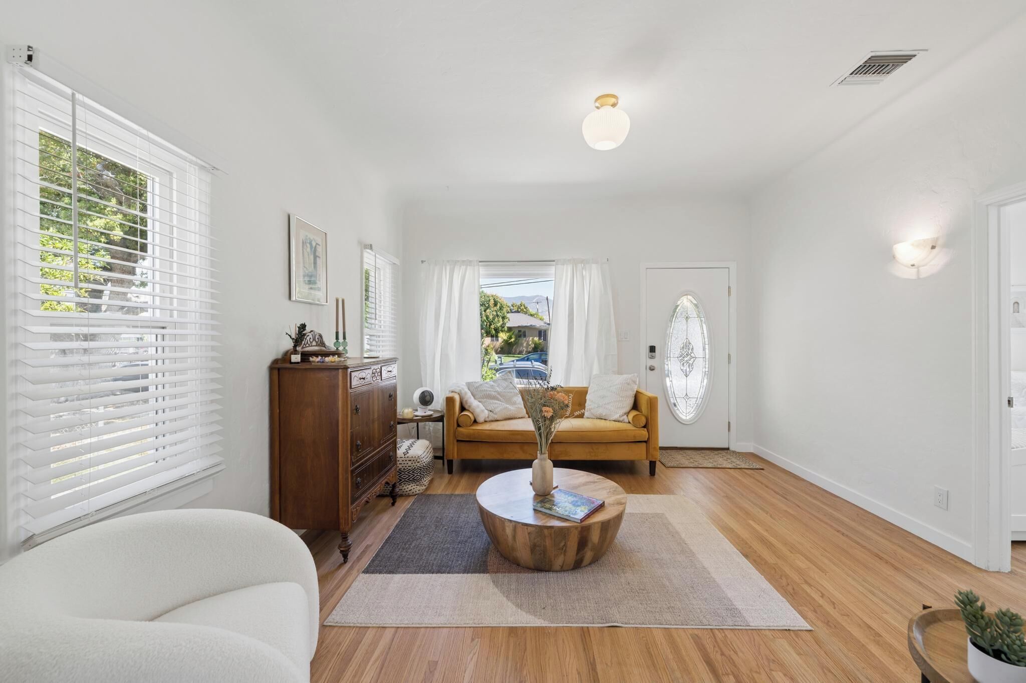 A spacious room with a wooden floor, a round coffee table, a sofa, a cabinet, and a door with a glass panel.