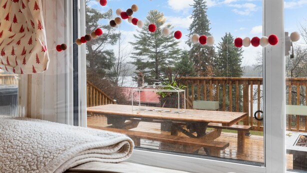 A room with a large window, a wooden deck outside, and a blanket on the bed.