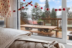 A room with a large window, a wooden deck outside, and a blanket on the bed. - Dahlia’s Waterfront Cottage in Denbigh (Denbigh)
