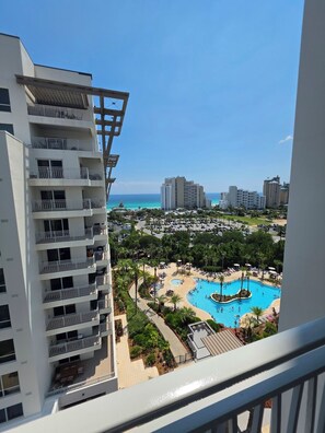 Ein Hochhaus mit mehreren Balkonen mit Blick auf eine Ferienanlage, die einen Pool und Meerblick bietet.