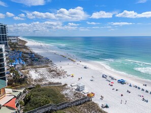 A beach with a boardwalk, umbrellas, and a building with balconies. - Luau 6901 Studio | 9th Floor South-Facing Gulf Views | 2 Queen Beds | Walk to Beach (Miramar Beach)