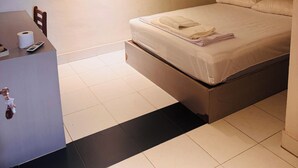 Habitación de hotel con cama, escritorio, silla, inodoro y una ventana pequeña.