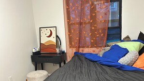 Een slaapkamer met een bed, een bureau met stoel, een lijst met afbeelding en een raam met gordijn.