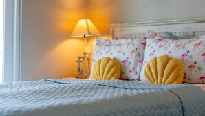 Una cama con cubierta acolchada, dos almohadas amarillas, una lámpara y una silla.