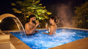 A hot tub with two people holding glasses, surrounded by trees and a night sky.