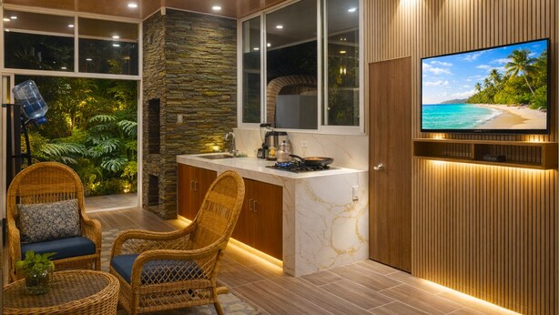 A modern kitchen with a stone accent wall, a built-in TV, and wicker furniture.