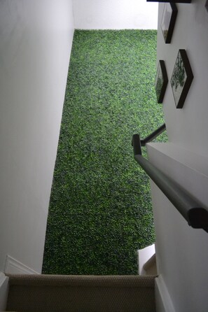 Un escalier recouvert d’un tapis en gazon synthétique vert, menant à un palier.