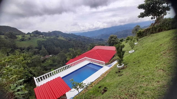 A pool with a red roof and white walls, surrounded by lush greenery and hills in the background. - El Mirador De Serrato (La Vega)
