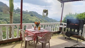 An outdoor dining area with a table set for two, a grill, and a scenic view of hills. - El Mirador De Serrato (La Vega)