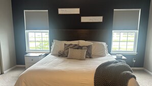 Un dormitorio con una cama grande, dos mesitas de noche, un ventanal y dos carteles en la pared.