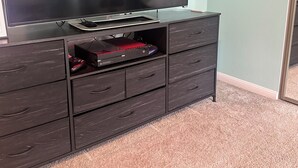 Un televisor de pantalla plana sobre un mueble de madera oscura con cajones, un control remoto de videojuegos rojo y un ratón.
