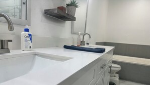 Un baño con un lavamanos blanco, un espejo, un estante con una planta en maceta y un inodoro.
