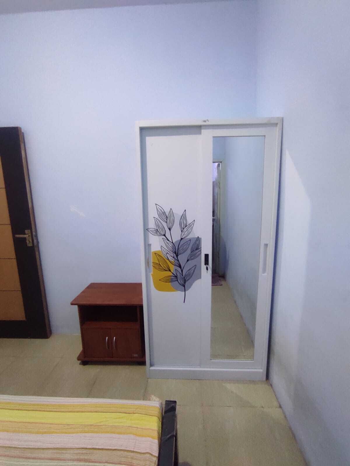 A bedroom with a wardrobe, a small wooden cabinet, and a bed with striped bedding.