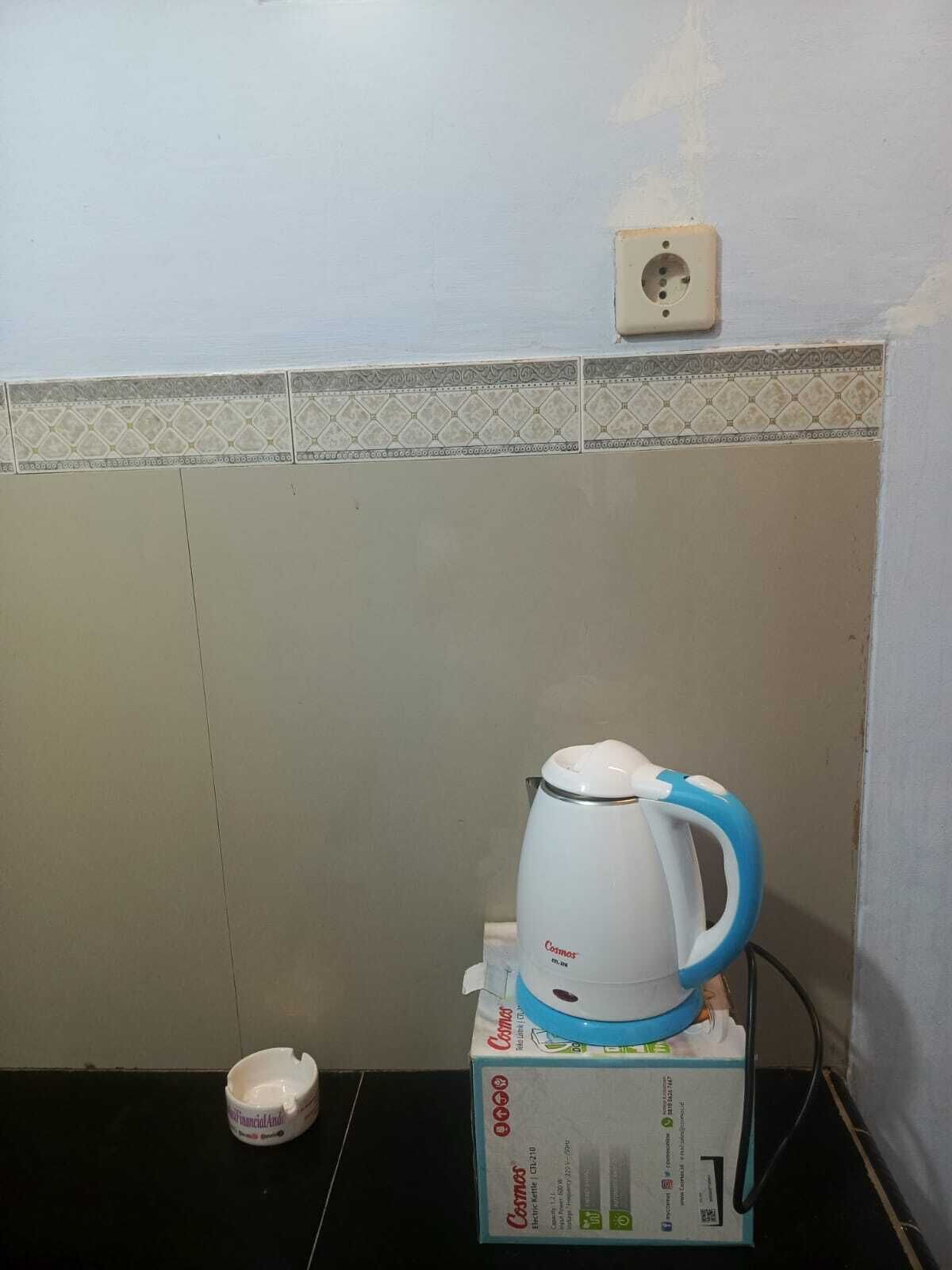 Una cucina con un bollitore bianco sopra una scatola, una ciotola piccola e una presa elettrica sulla parete.