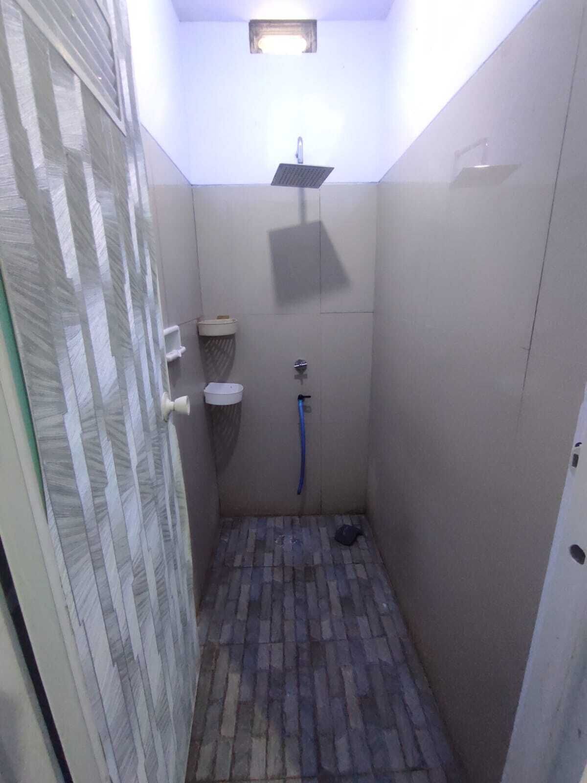 Ein kleines Duschbad mit Fliesen, einem Waschbecken und einem blauen Duschschlauch.