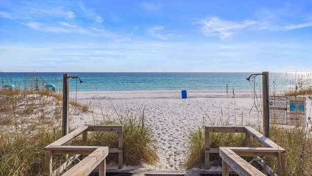 Una spiaggia con passerelle di legno che conducono all'acqua, sabbia dorata e cielo azzurro.