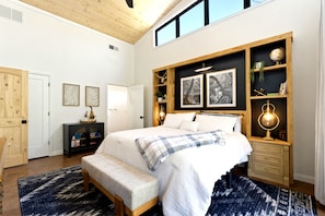 A bedroom with a large bed, wooden headboard, built-in shelves, a bench, and a large window. - Modern creekside cabin on 32 private acres. 15 minutes from Buffalo Trace! (Frankfort)