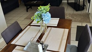 A living room with a dark-colored sofa set, a coffee table, a TV stand, and a dining area with a table and chairs.