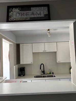 Una cocina con armarios blancos, un grifo negro, una cafetera y un cartel enmarcado sobre el fregadero.