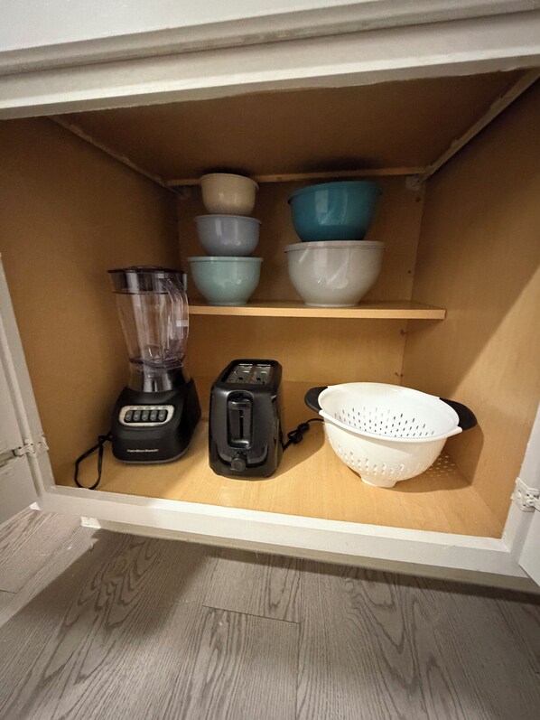 Un armario de cocina con una licuadora, un tostador y tazones apilados.