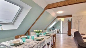 Et spiseområde med et bord dækket til fire personer, ovenlys og et sovehems med seng og knagerække.