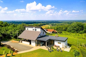 A modern house with a large patio, a covered outdoor area, and a view of a green landscape. - Modern home with jacuzzi, sauna, wellness and kids’ playground (Grabrovnik)