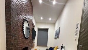 Una habitación con chimenea de ladrillo, un sofá gris, una pequeña mesa y piso de madera.