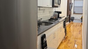 Una cocina moderna con armarios blancos, un refrigerador de acero inoxidable, un microondas y suelo de madera.