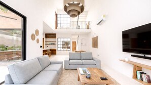 Un salon moderne avec un canapé d’angle, une table basse, un téléviseur et un balcon agrémenté de plantes.